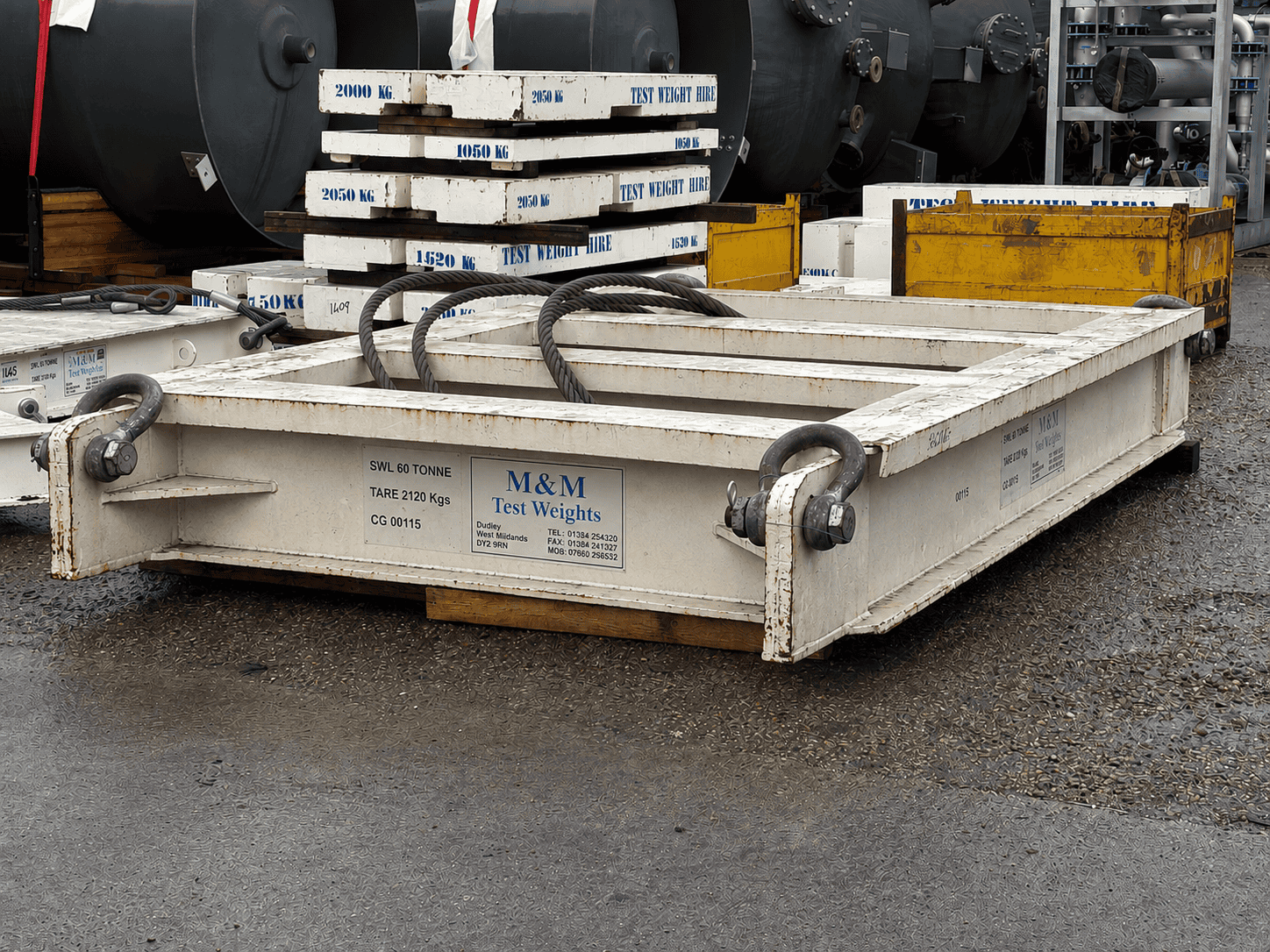 Industrial M&M test weights platform with stacked weights and lifting cradle.