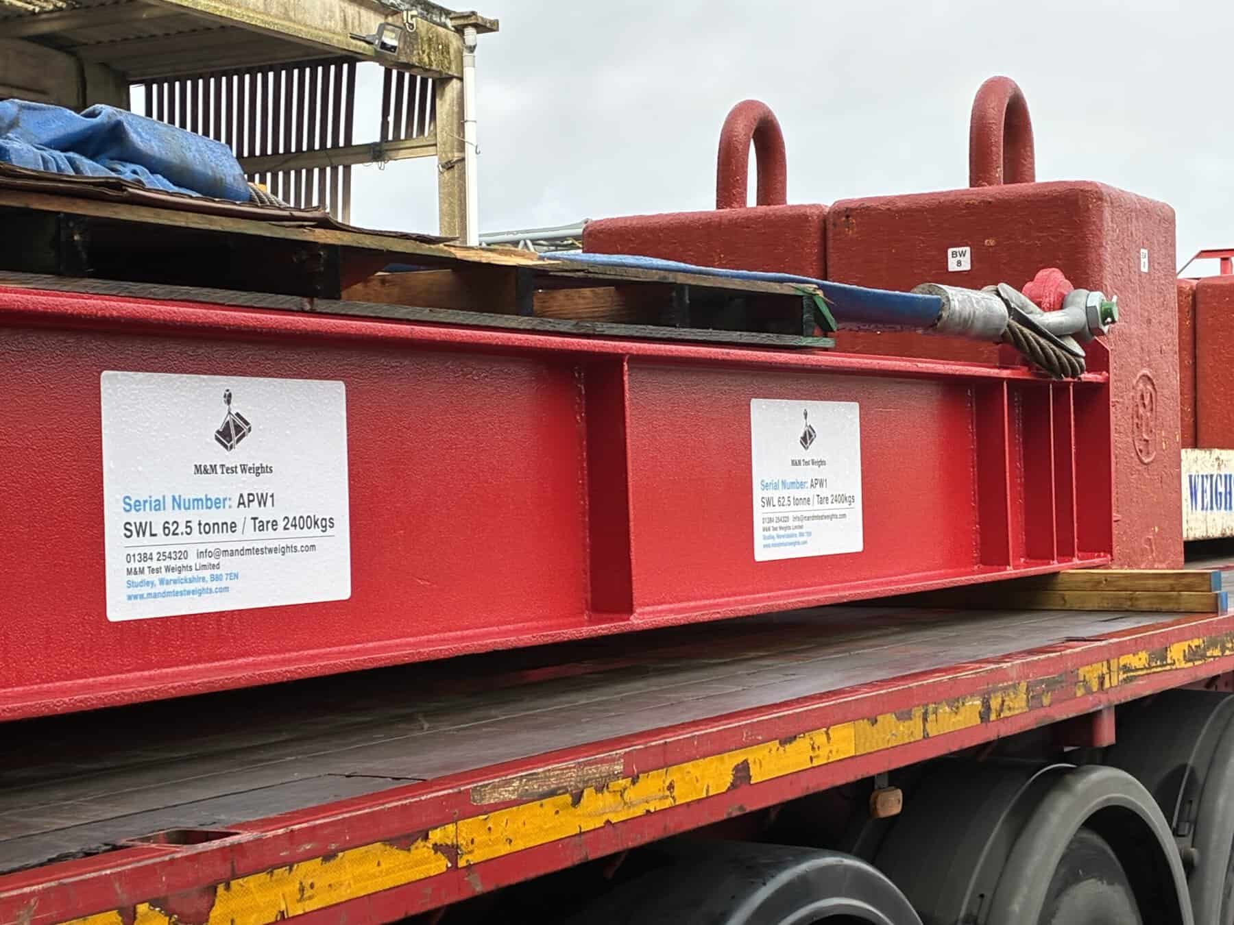 Red lifting cradle with test weights and serial labels for crane calibration.