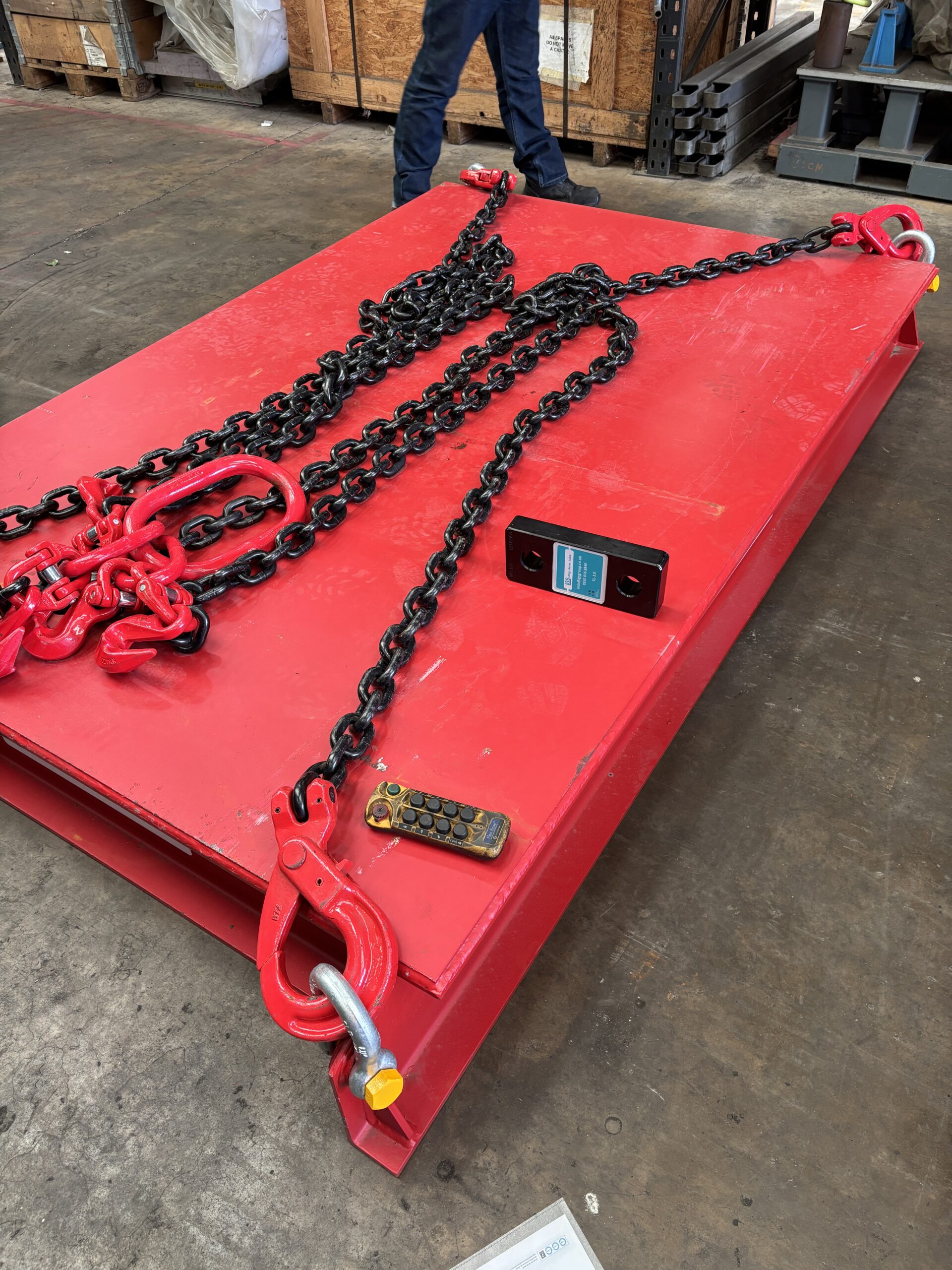 Red lifting cradle with chains and hooks for industrial weight testing.